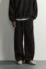 Pantalón jogger de corte relajado en color negro, confeccionado en tejido con elasticidad. Presenta cintura elástica con cordón ajustable y bolsillos laterales decorados con tachas metálicas.