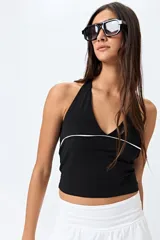 Top halter negro con escote en V y detalle de vivo blanco horizontal. Presenta un diseño ajustado al cuerpo y espalda descubierta con tiras regulables.