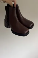 Botines de cuero vacuno en color marrón, con diseño de caña media, taco cuadrado y plataforma delantera. Presentan una combinación de texturas en el cuero y un estilo robusto.