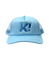 Gorra tipo trucker color celeste con panel frontal rígido y paneles traseros de malla. Presenta un bordado frontal con la letra K y una estrella, además de un bordado lateral con la marca.
