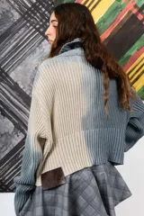 Saco de hilo con cuello alto y cierre de botones, de tejido de punto y diseño oversize. Presenta un teñido artesanal degradado que combina gris y beige, con mangas largas y puños amplios, además de un detalle de aplicación floral oscura en el pecho.