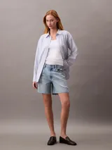 Short de jean de tiro alto con diseño de cinco bolsillos, cierre de cremallera y botón, con detalles de roturas y ruedo deshilachado.