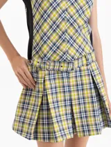 Vestido corto sin mangas con estampado de cuadros escoceses en tonos verde, amarillo y azul. Presenta un diseño ajustado en el torso con paneles laterales negros, falda tableada con vuelo y cinturón integrado con hebilla en la cintura.