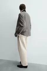Pantalón chino de corte relajado, confeccionado en tejido estructurado de color beige. Presenta bolsillos frontales, bolsillos traseros de vivo y cierre frontal con cremallera y botón.