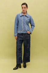 Chaqueta de lana merino hervida en color marrón, con diseño estructurado y cuello amplio. Presenta detalles de bordado artesanal en contraste color mostaza a lo largo del frente, cuello y puños, junto con botones forrados en la misma tela.