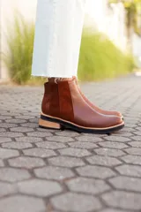 Botas tipo Chelsea de cuero, con diseño de paneles combinados en texturas lisas, gamuzadas y con relieve tipo reptil en el talón. Presentan una suela plana con taco bajo de madera y base de goma negra.