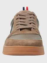 Sneaker de hombre en tonos marrones, confeccionada en una combinación de cuero y descarne. Presenta un diseño de paneles con cordones al tono, suela de goma color caramelo y un detalle de cinta tricolor en el talón.