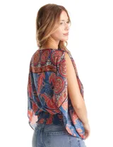 Blusa de gasa con estampado de arabescos en tonos azules y rojos, con cuello a la base y mangas tipo capa. Presenta una silueta holgada con ruedo elástico en punto smock que ajusta a la cintura.