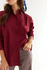 Camisa de corte oversize color bordó, con cuello camisero, mangas largas y bordado en hilo rojo en la espalda con la frase The Winter League. Presenta recortes con costuras a contratono y detalle de placa metálica pequeña en la parte superior trasera.