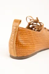 Zapatos planos de cuero color caramelo, con textura trenzada, cordones frontales en el empeine y punta redondeada.