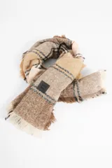 Pashmina de formato cuadrado con diseño de cuadros escoceses en tonos negro, rojo, verde y amarillo. Presenta terminaciones con flecos en sus bordes y una pequeña etiqueta decorativa.