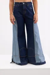 Pantalón wide leg de tiro alto confeccionado en denim de diseño bicolor, combinando tonos azul oscuro y celeste con costuras en contraste. Presenta bolsillos tipo parche en la parte inferior de las piernas y aberturas en los puños.