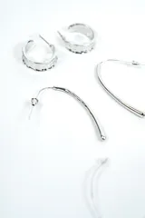 Set de tres pares de aros plateados de diseño variado, incluyendo aros de argolla texturados, aros colgantes alargados y aros con dijes en forma de medialuna.