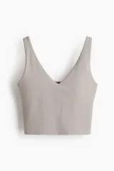 Top deportivo de sujeción media, color gris claro, con escote en V pronunciado y breteles anchos. Presenta copas forradas con relleno extraíble y elástico revestido en el bajo.