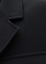 Chaqueta negra de corte recto con cuello de solapa, cierre frontal con botones y cinturón integrado. Presenta cuatro bolsillos de parche en la parte delantera y mangas largas.