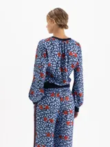 Camisa de viscosa con diseño estampado de corazones rojos sobre fondo azul con manchas. Presenta cuello redondo, puños y ruedo tejidos en ribb, con mangas largas abullonadas y hombros caídos.