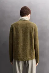 Sudadera de ajuste regular, color verde oliva, con cuello redondo y manga larga. Presenta una textura irregular en el tejido, similar al borreguito o bouclé.