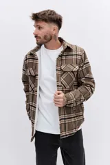 Campera tipo sobrecamisa de franela a cuadros en tonos marrones y beige, con interior forrado en corderito blanco. Presenta cierre frontal, bolsillos en el pecho con solapa y mangas largas con puños abotonados.