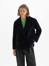 Tapado de paño azul marino con corte cruzado y doble botonadura. Presenta bordados de bocas en hilo rojo distribuidos por toda la prenda y detalles de flecos en los bordes de la solapa y el cuello.