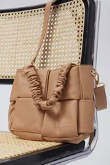 Cartera tipo tote bag color tostado, con diseño acolchado de bloques, manija fruncida y correa ajustable y desmontable.