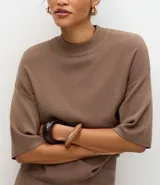 Blusa de punto de corte holgado, color negro, con cuello redondo elevado y mangas cortas amplias con sisa desplazada.