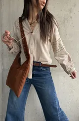 Camisa beige de inspiración boho con detalles bordados en mangas y puños, cuello en V con botones frontales y mangas largas abullonadas.