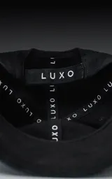 Gorra de gabardina negra con visera curva y bordado frontal en hilo rojo con la palabra "Ravers" en tipografía cursiva. Posee ajuste trasero de velcro.