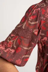 Blusa de viscosa color marrón con estampado floral en tonos rosados y rojos, de corte oversize, cuello en V con detalles de encaje y mangas largas abullonadas con inserciones de encaje.