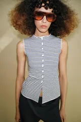 Top tipo chaleco confeccionado en hilatura con viscosa, con diseño de rayas horizontales en blanco y azul marino. Presenta cuello redondo, manga sisa y cierre frontal con botones.