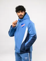 Campera de abrigo Umbro del Club Nacional de Football, con diseño de bloques de color en azul, blanco y rojo. Cuenta con capucha ajustable, cierre frontal y logo de la marca junto al escudo del club en el pecho.