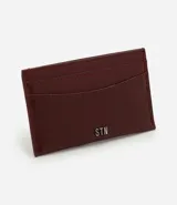 Billetera compacta de poliuretano color bordó, de diseño slim con compartimentos para tarjetas y aplicación metálica frontal con el logo de la marca Satinato.