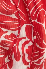 Vestido largo de tejido ligero color blanco con estampado floral rojo. Tiene cuello redondo con lazos, mangas globo largas con puños abotonados, corte holgado y falda con volantes en el ruedo.