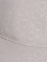 Gorra de béisbol color beige claro con patrón jacquard repetitivo del logo 'CK'. Presenta visera curva y cierre ajustable trasero con herrajes de la marca.