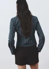 Blusa de algodón con diseño entallado y patrón de cuadros, cuello camisero, manga larga con puños abotonados y cierre frontal de ganchos con detalles fruncidos.