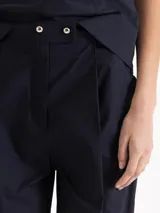 Pantalón slouchy de poplín color beige, de calce regular y largo al tobillo, con tablas en el delantero y ruedo que aportan volumen, bolsillos laterales y cierre con botones tipo honguito.