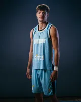 Camiseta de básquet celeste con cuello y sisas en azul marino. Estampado frontal con la palabra "Uruguay" en blanco y el logo de Antel. Incluye logo de Umbro y el escudo de Uruguay. No incluye número ni parche.