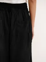 Pantalón negro de lino con cintura elástica fruncida y pernera ancha, con detalles de cordones ajustables a los lados.