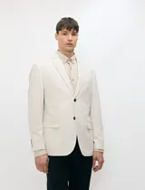 Blazer de medio forro color beige, confeccionado en mezcla de algodón y lino. Presenta una silueta estructurada con solapas de muesca, cierre frontal de un botón y bolsillos con solapa.