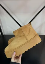 Botas cortas de gamuza color tostado con plataforma plana y suela dentada. Presentan un diseño minimalista con costuras reforzadas y forro interior de peluche.
