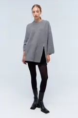 Sweater gris de punto grueso con cuello redondo y mangas largas. Tiene corte holgado y cierre lateral con cremallera.