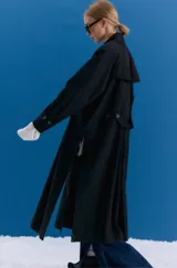 Trench midi de color negro, confeccionado en una mezcla de algodón y nylon con propiedades repelentes al agua. Presenta un diseño holgado con tajos laterales, bolsillos internos y detalle de etiqueta en la espalda.