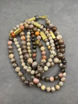Collar de cuentas de piedras naturales en tonos tierra, con detalles de tubos dorados en los laterales.
