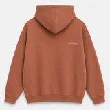 Canguro con capucha de calce oversize, confeccionado en tejido pesado color gris claro. Presenta un bordado minimalista con la palabra 'ASCEND' en la parte superior trasera, puños y ruedo acanalados.