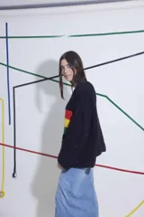 Sweater tejido de lana color negro con rayas horizontales en rojo, amarillo y verde. De corte holgado y mangas largas.