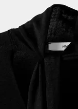 Jersey de punto fino color negro, con cuello en pico y detalle de fular integrado en el escote. Presenta un diseño recto y mangas largas.