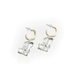 Aros colgantes con base circular color crema y dije de acrílico transparente con forma irregular.