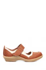 Zapato tipo guillermina de cuero, con diseño combinado en tonos marrón y beige. Presenta cierre con tira de velcro en el empeine, costuras decorativas visibles y suela plana de goma en color tostado.