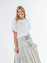 Remera blanca de tejido liviano con aplique de flor de crochet en el frente.