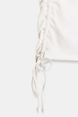 Camiseta corta de cuello redondo y manga corta, color gris oscuro, con frunces laterales ajustables mediante cordones.