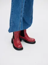 Bota tipo chelsea de cuero vacuno en color rojo con estampado floral grabado en negro. Presenta paneles laterales elásticos, suela de plataforma y taco cuadrado en color negro.